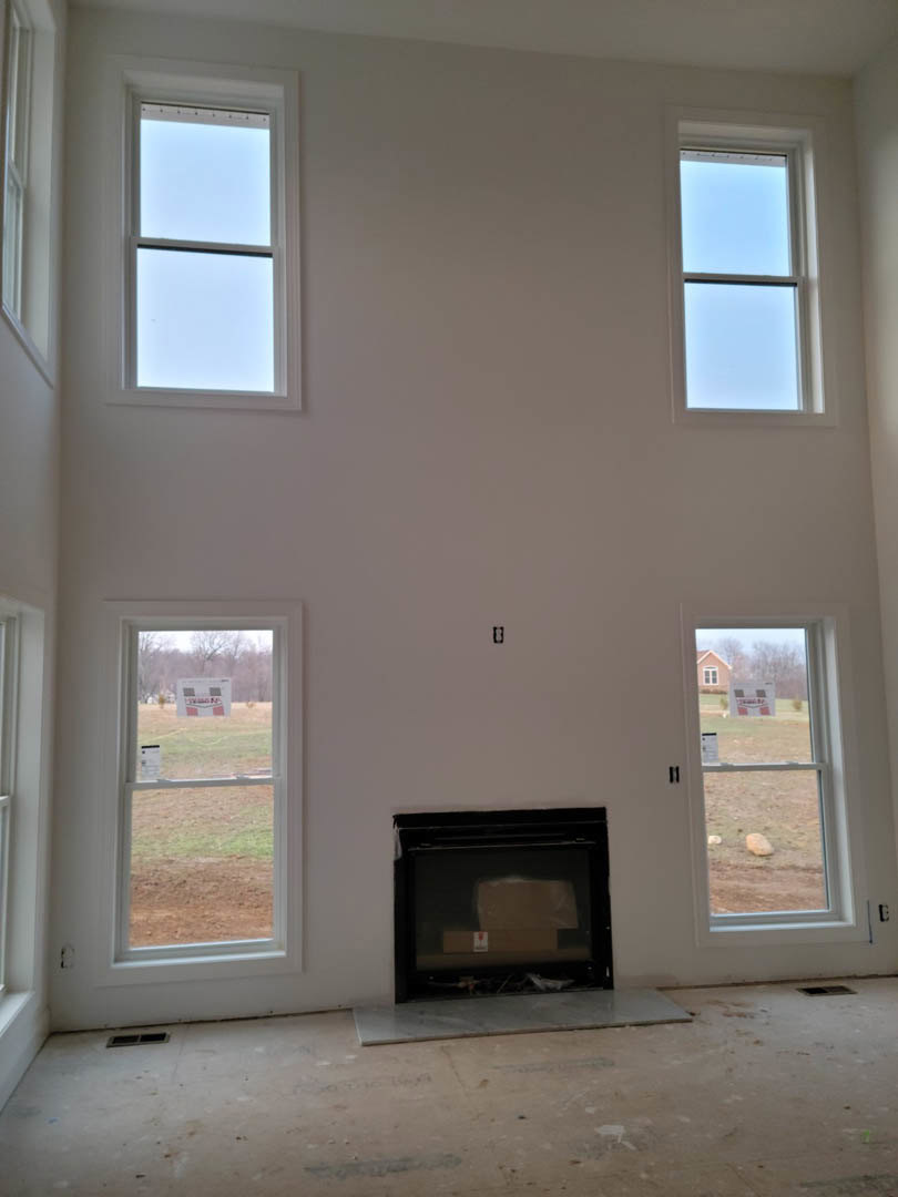 Stone fireplace with glass doors, surrounded by large white-framed windows, hardwood flooring, and neutral painted walls in a living room.