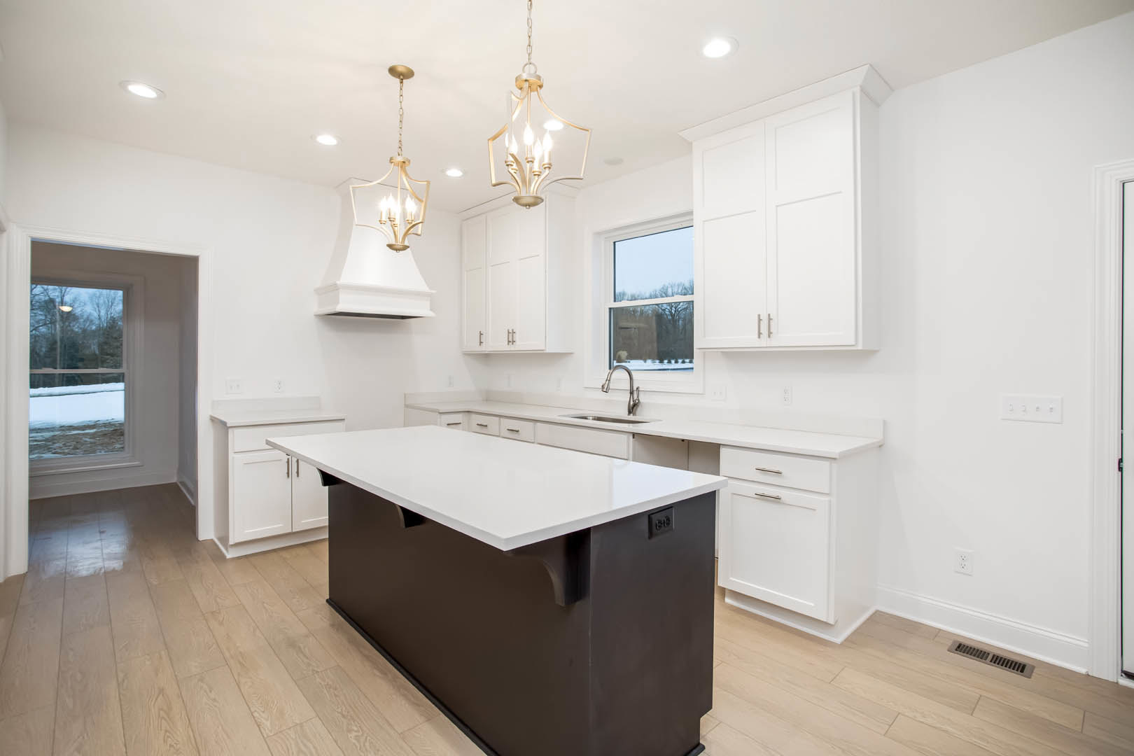 White kitchen cabinets, black island with white countertop, pendant light fixture, window overlooking snowy trees, white dining table
