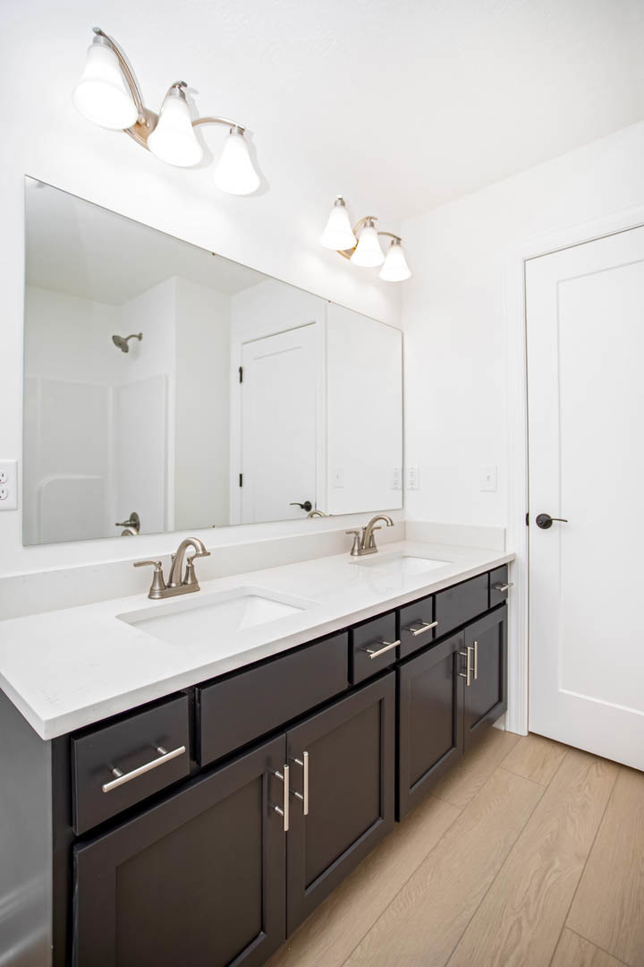 Bathroom with white double vanity, quartz countertop, two undermount sinks, chrome faucets, large framed mirror, three-light fixture above, light gray tile floor, shaker-style