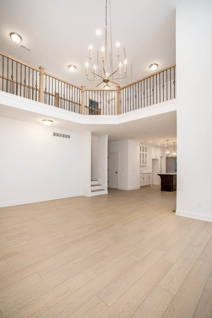 Spacious living area with hardwood floors, central staircase featuring wood railings, and ornate chandelier hanging from a plaster ceiling