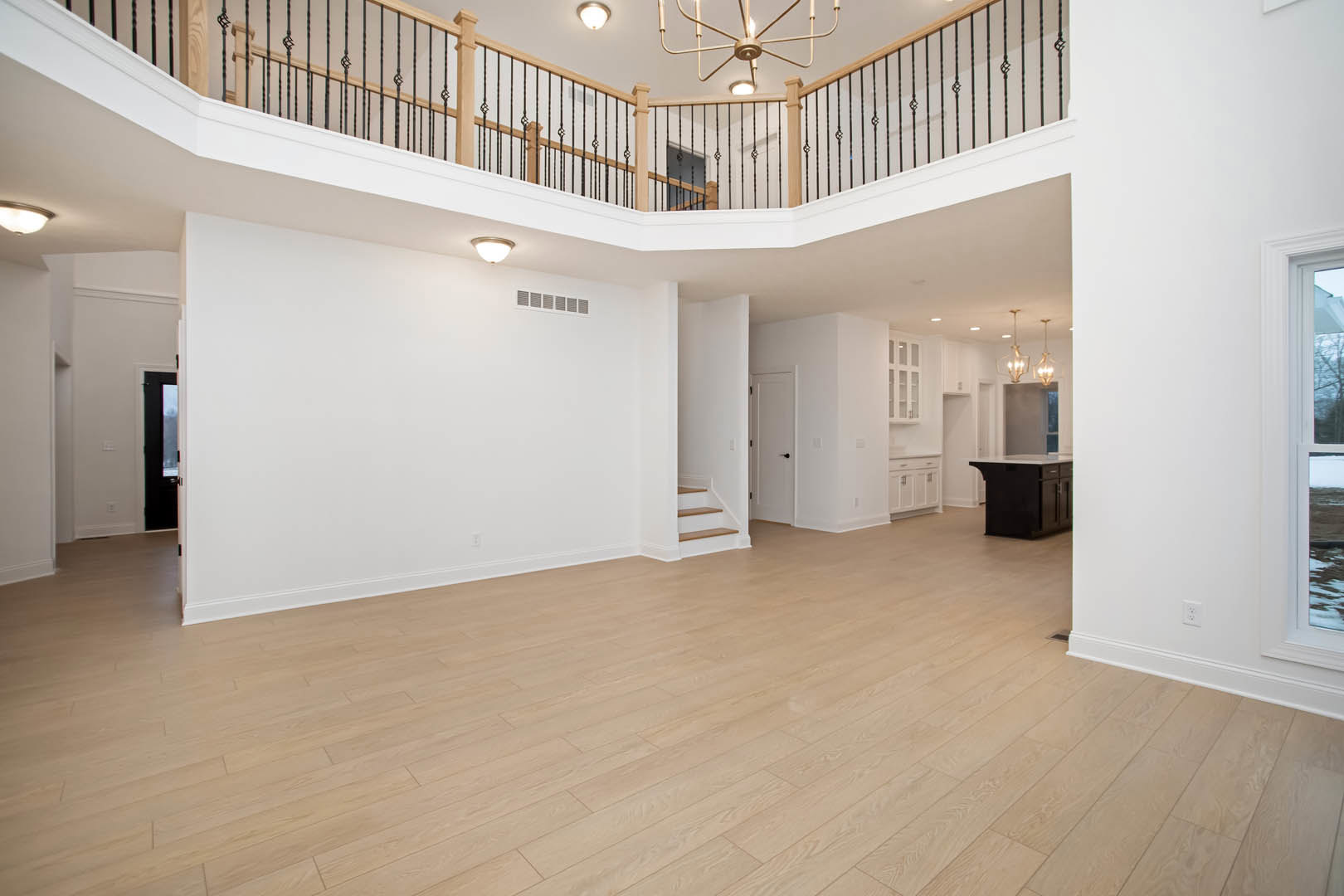 Spacious room featuring wood flooring, prominent staircase with white walls, ceiling fan and light fixture, window with white frame, and decorative molding.