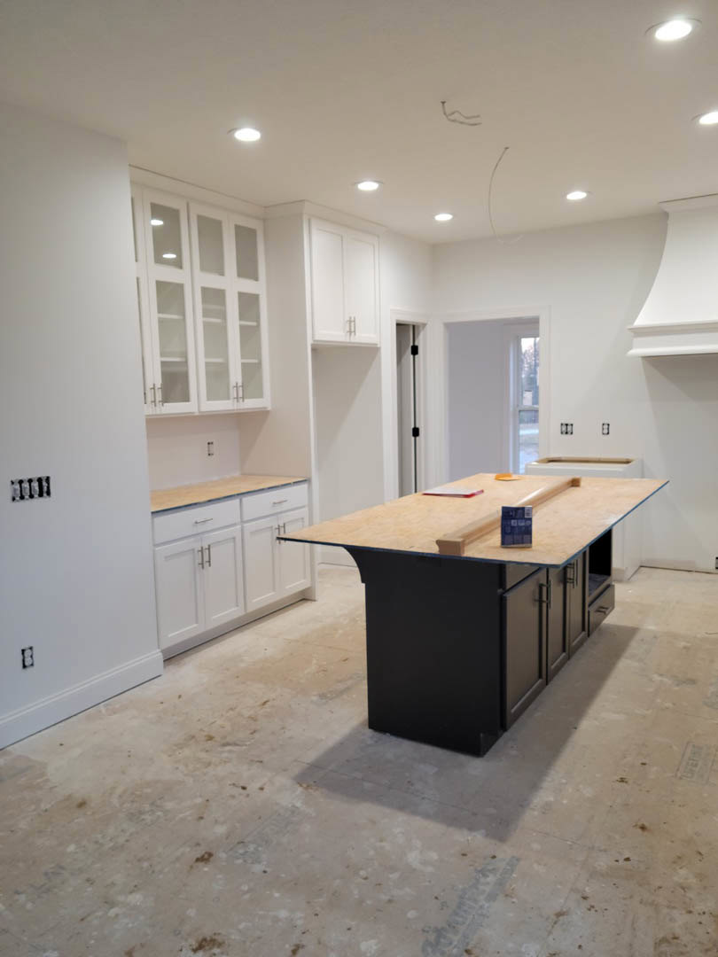 Modern kitchen featuring a central island with a light stone countertop, white cabinetry, tile backsplash, stainless steel sink, and smooth white walls.