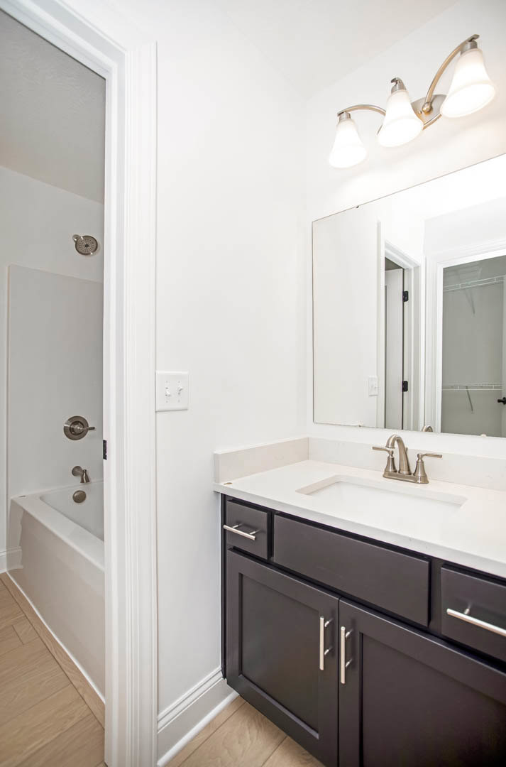 Bathroom with freestanding bathtub, white sink on stone countertop, wood flooring, white walls, modern light fixture, and white door