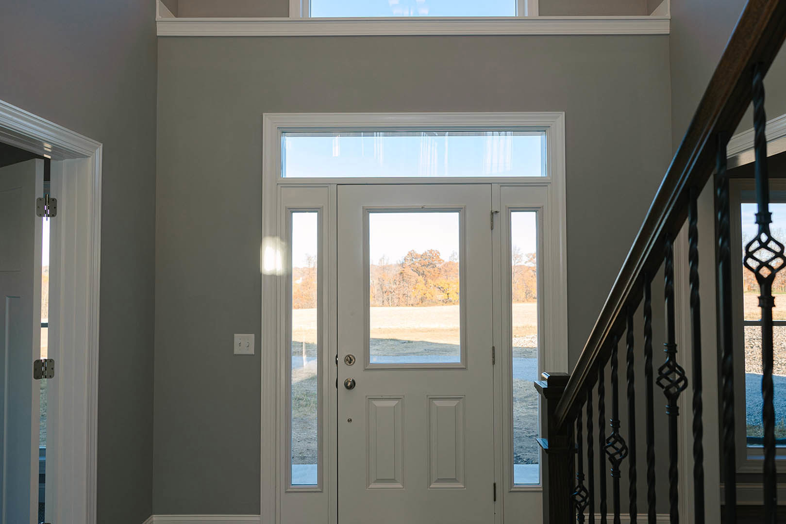 White door with glass panes and silver handle, positioned beside a staircase with wooden treads and white risers; light switch on adjacent wall, daylight streaming through window