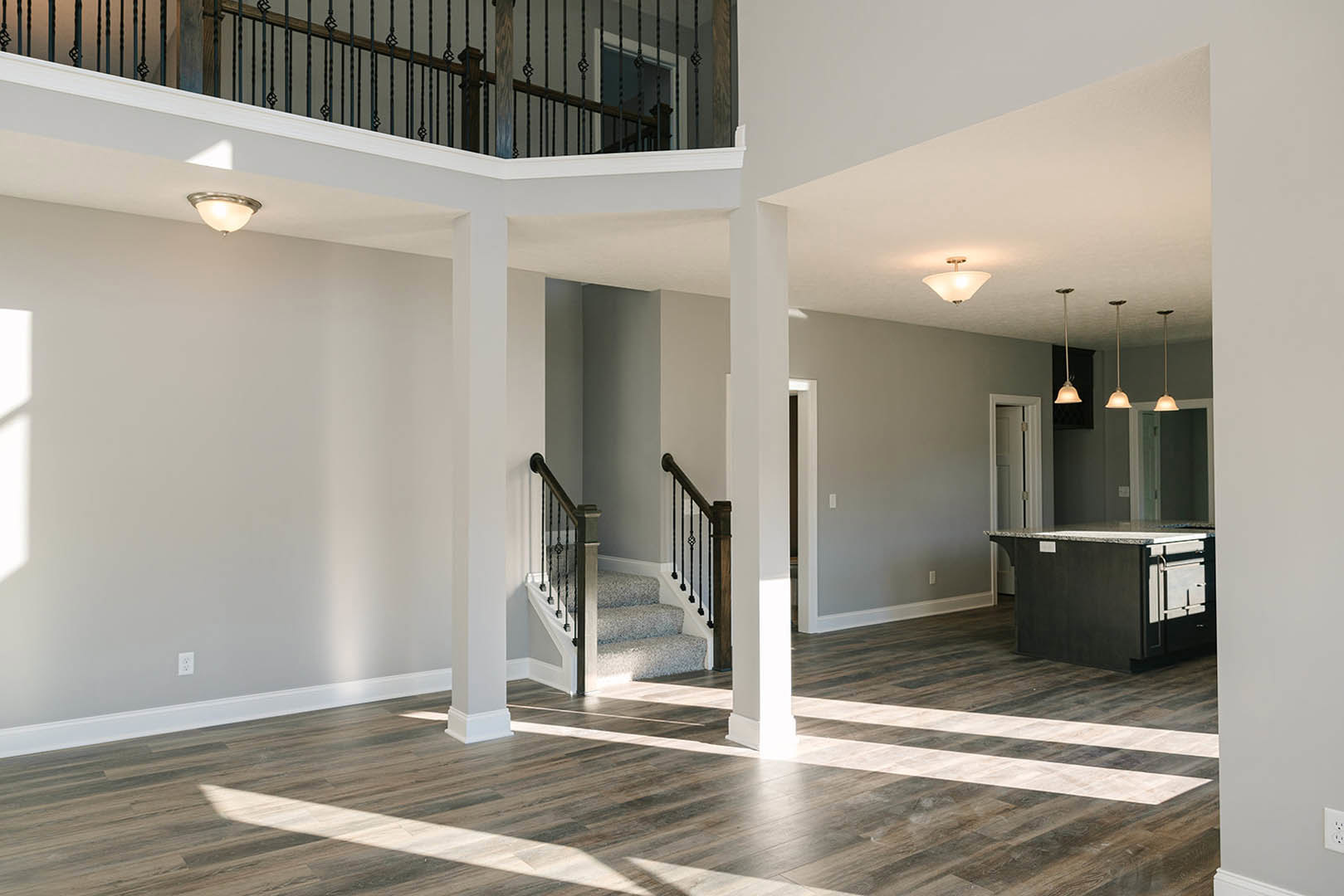 Open-concept kitchen with marble island, wooden floors, modern staircase, and ceiling light fixtures illuminating the space