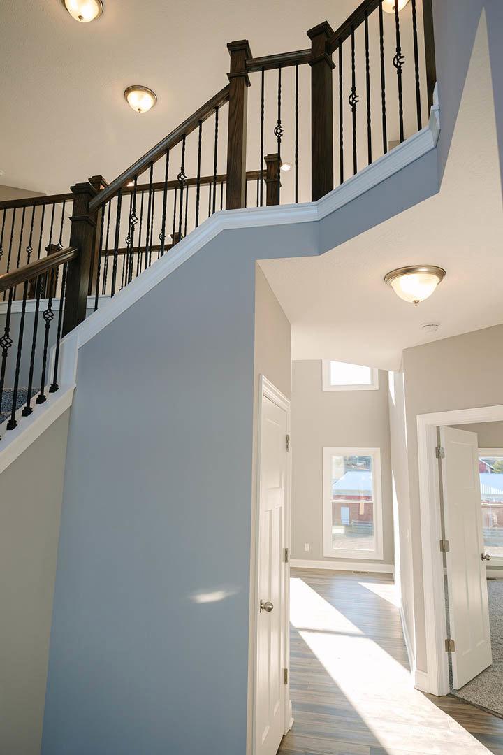 Wooden staircase with white balusters, modern light fixture on ceiling, window with white trim, natural light illuminating hardwood floor, close-up of metal railing and paneled