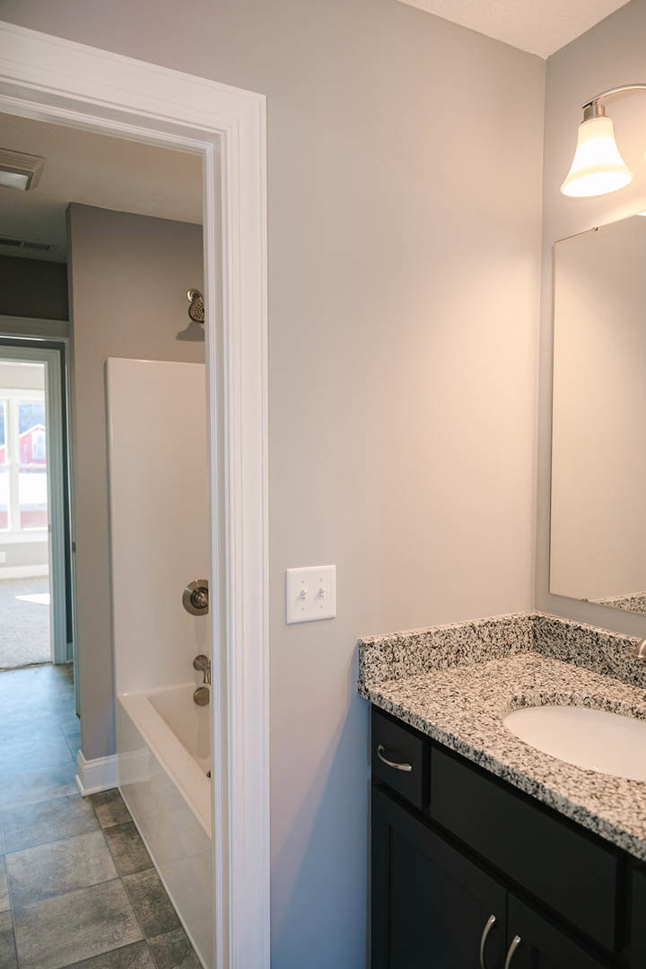 Modern bathroom with white tile walls, rectangular sink on a stone countertop, chrome faucet, glass-enclosed shower, dual white light switches, and window overlooking a red