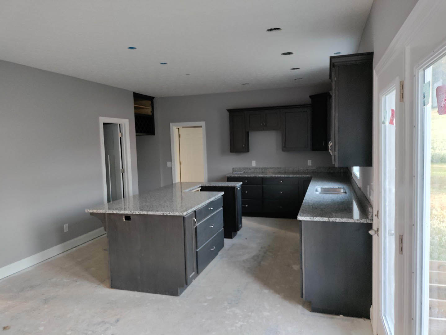 Granite countertops and wood cabinets in a modern kitchen with a central island featuring a cutout, white door with matching frame, and stainless steel sink fixtures.