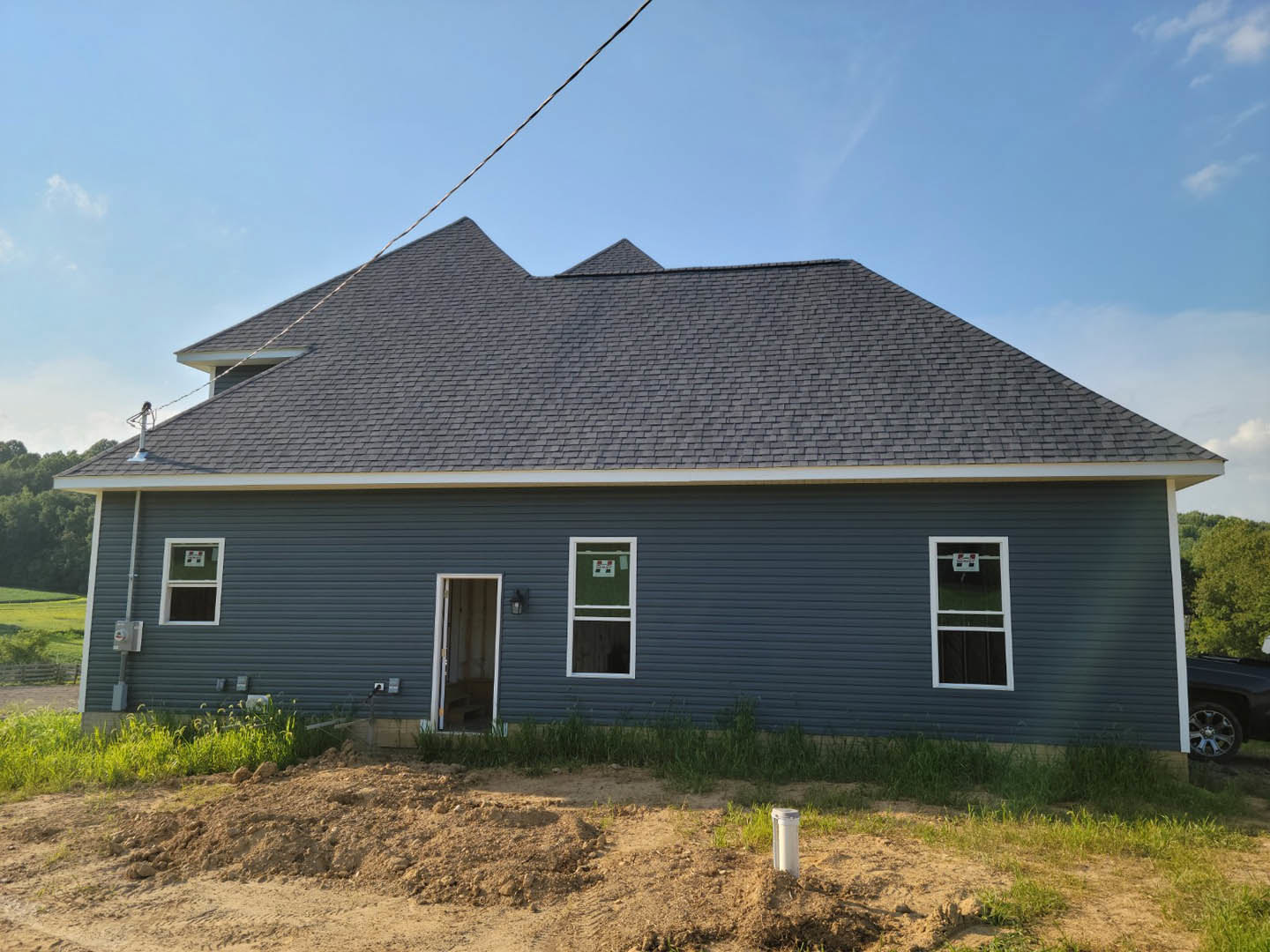 Two-story home with open front door, white-framed windows, gray siding, and a dirt patch bordered by sparse grass in the yard