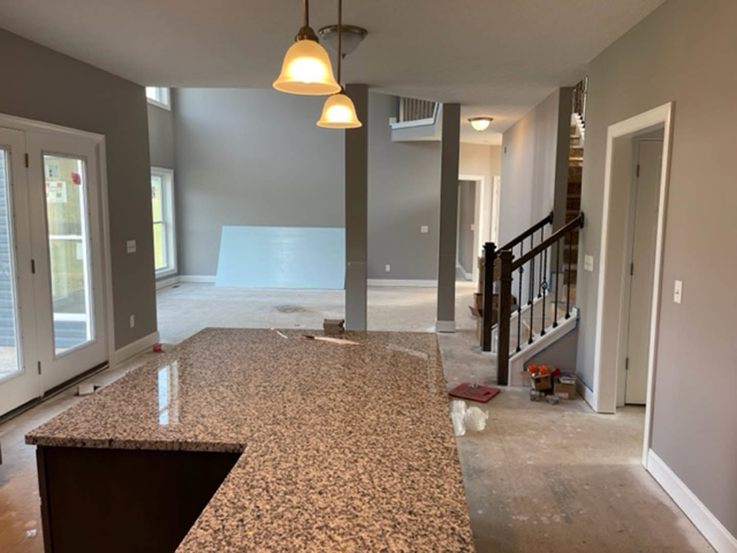 Modern kitchen with white tile backsplash, light wood laminate flooring, quartz countertop, glass window, recessed lighting, and adjacent staircase with plaster walls
