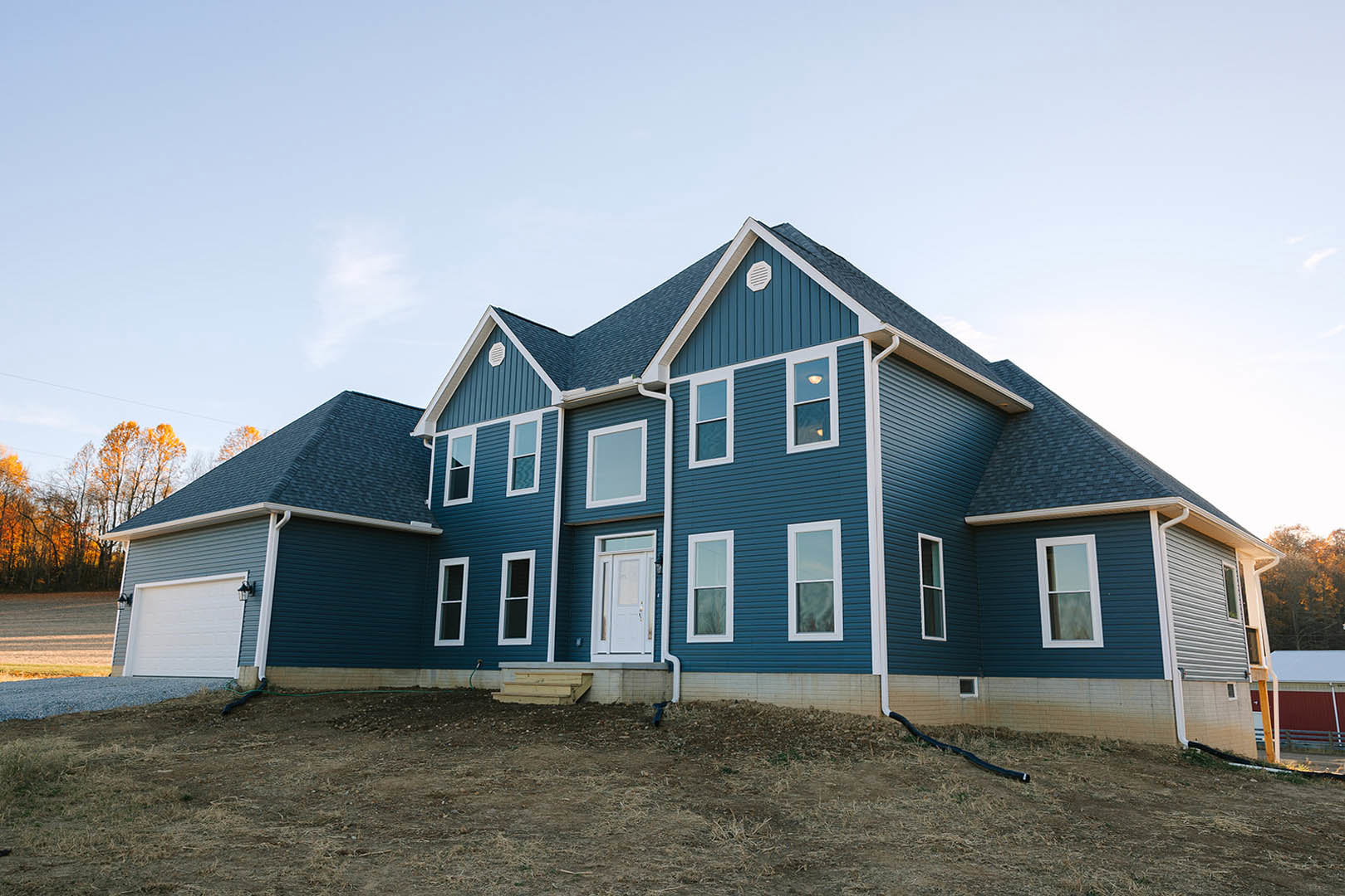 Blue roof with white trim, white-framed window illuminated from inside, glass-paneled white door, light gray siding, mature tree in front yard