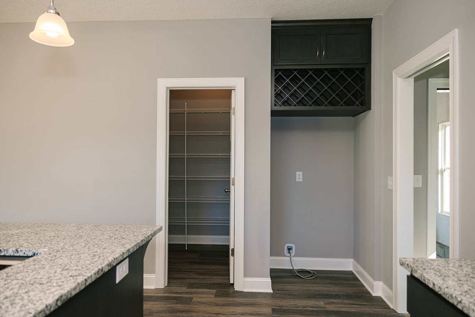 Modern kitchen with open door, tile flooring, white plaster walls, black floating shelf, light fixture with exposed bulb, built-in cabinetry, countertop close-up, closet with