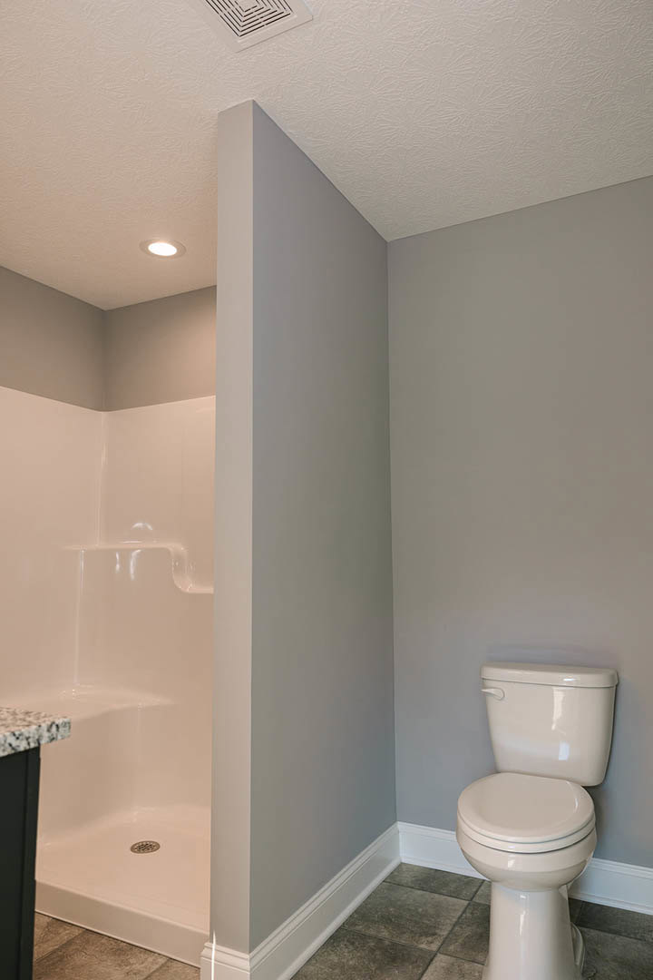Modern bathroom with white toilet, glass shower enclosure, light tile flooring, plaster walls, and black corner accent