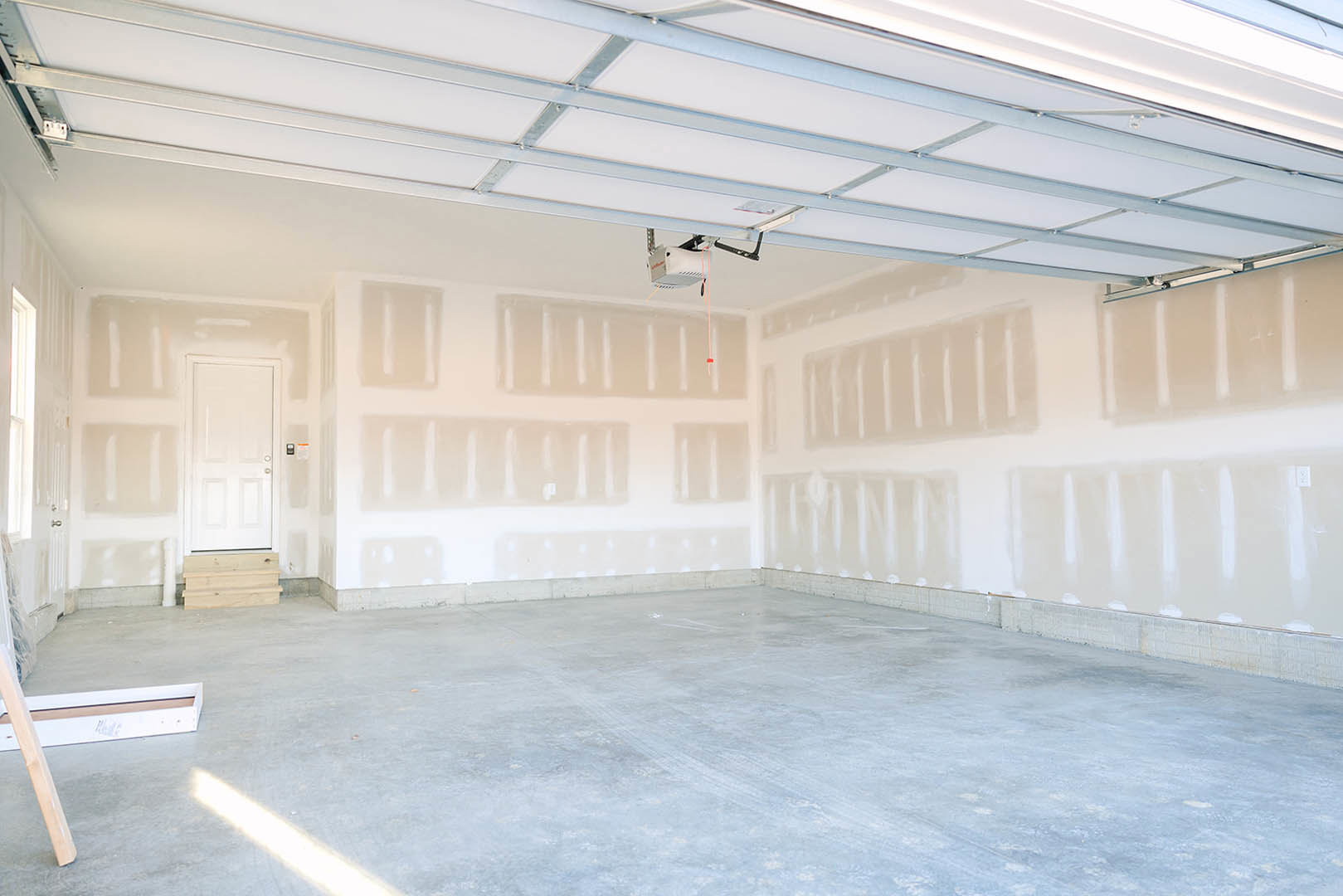White walls and ceiling, white door with matching frame, concrete floor, wood panel detail, wooden furniture leg against white background.