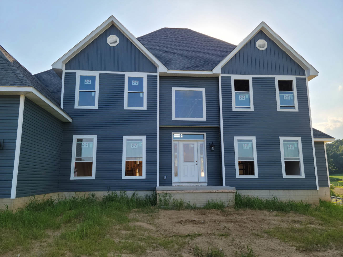 Blue metal roof cottage with white siding, white framed window, white door with glass insert, grassy front yard, white vent on exterior wall