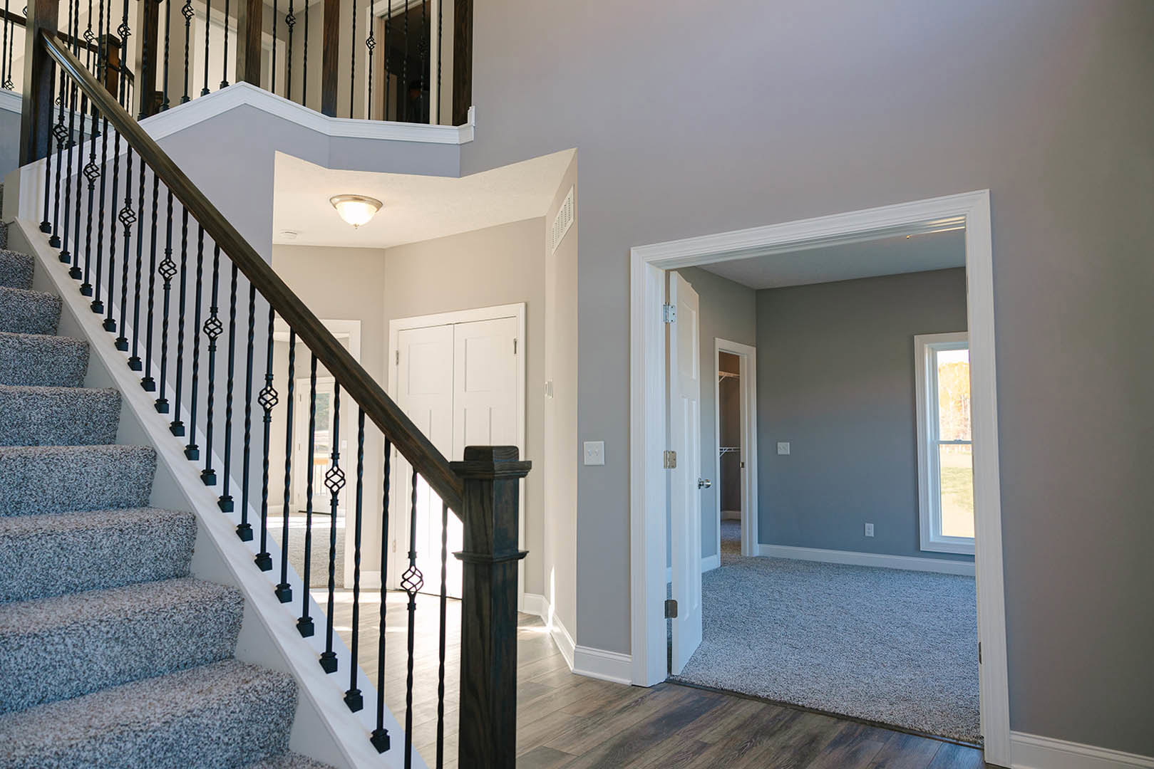 Carpeted staircase with black metal railing, large window overlooking open field, modern ceiling light fixture, white walls