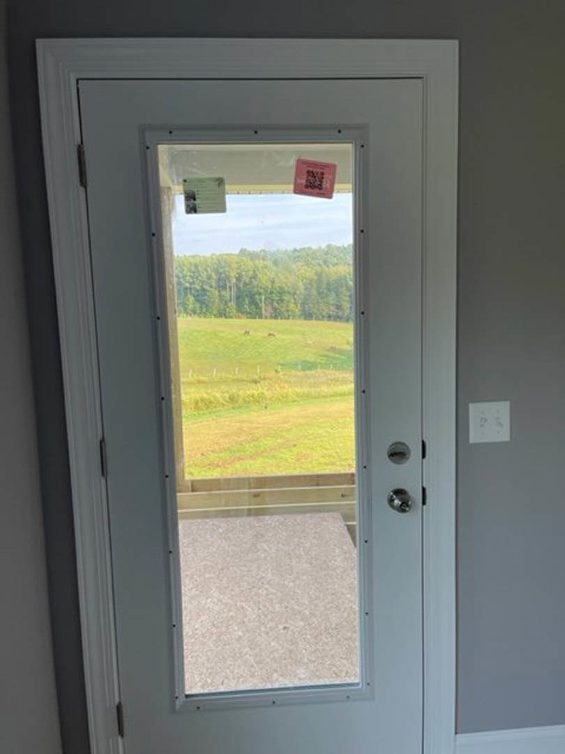 Wooden door with glass panels opening to grassy field and trees, silver door handle, white interior trim