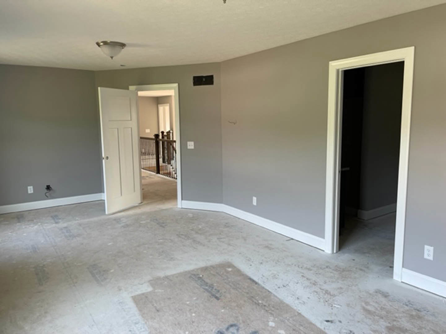Open white door with silver doorknob, white baseboards, staircase with dark railing, neutral walls, and ceiling light fixture