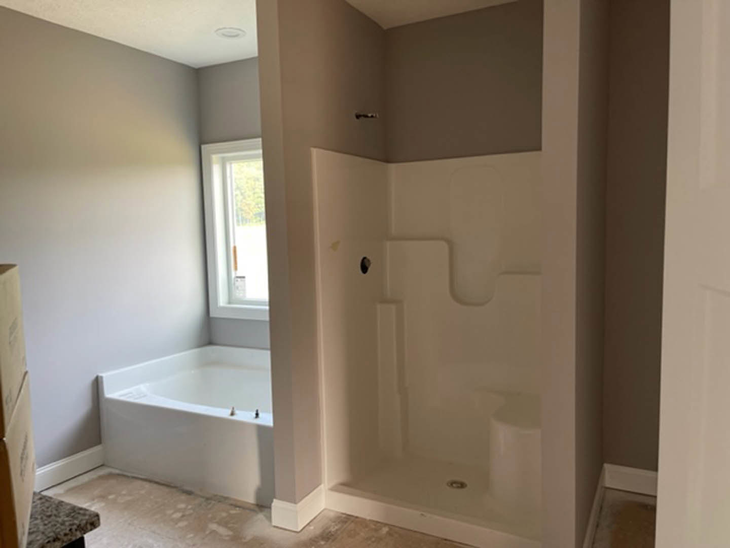 Freestanding white bathtub beside glass-enclosed shower, light plaster walls, wood door, and tile flooring in modern bathroom