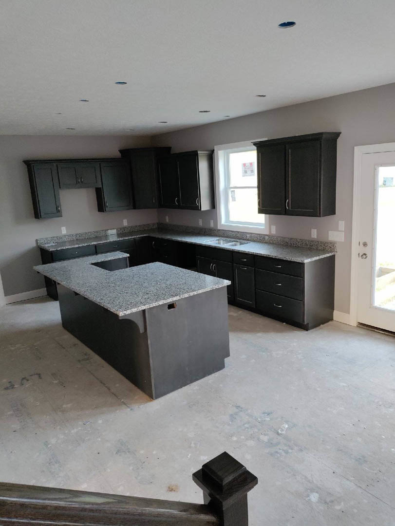 Black kitchen cabinets with polished granite countertops, stainless steel sink, light-colored tile floor, and neutral walls