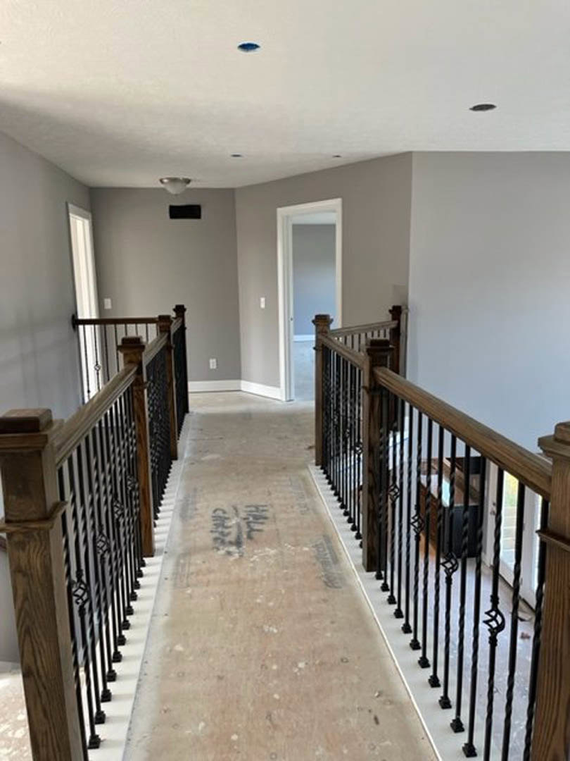 Hallway with black metal railing, light wood floors, white plaster walls, and recessed ceiling lighting