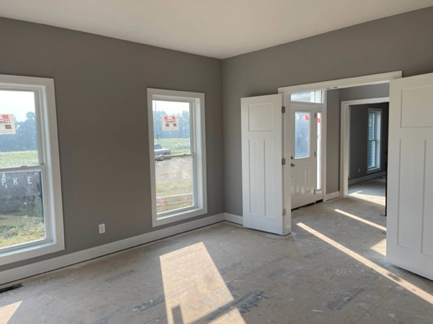 Bright room featuring white paneled doors, large windows with white trim, light-colored flooring, and smooth white walls.