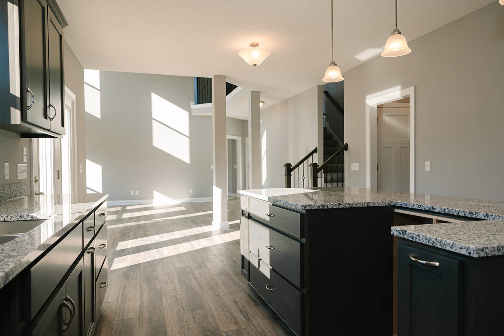 Marble island with waterfall edge, white cabinetry, stainless steel sink, pendant lights, and hardwood flooring in a modern kitchen
