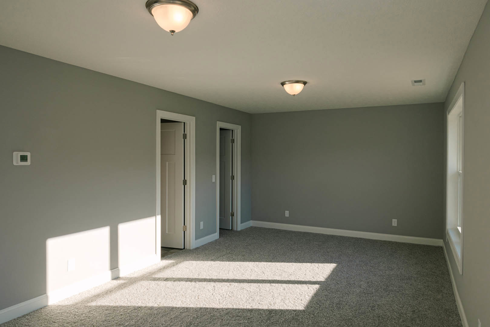 Bright carpeted room with white walls, recessed ceiling light, and wooden door.