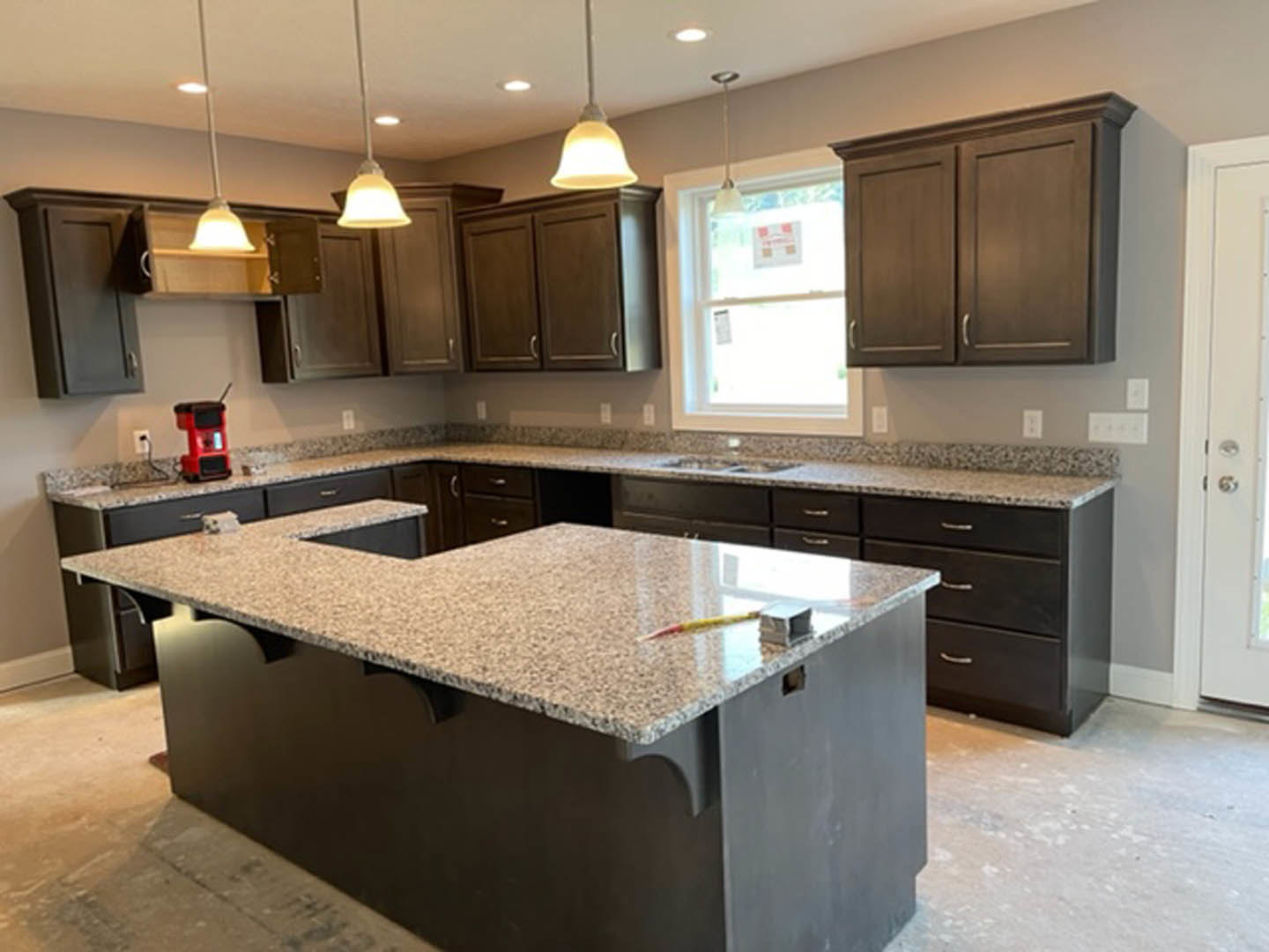 Granite kitchen countertops with tile backsplash, white cabinetry, stainless steel sink, and a window displaying a sign; pencil resting on counter, close-up views of cabinet and