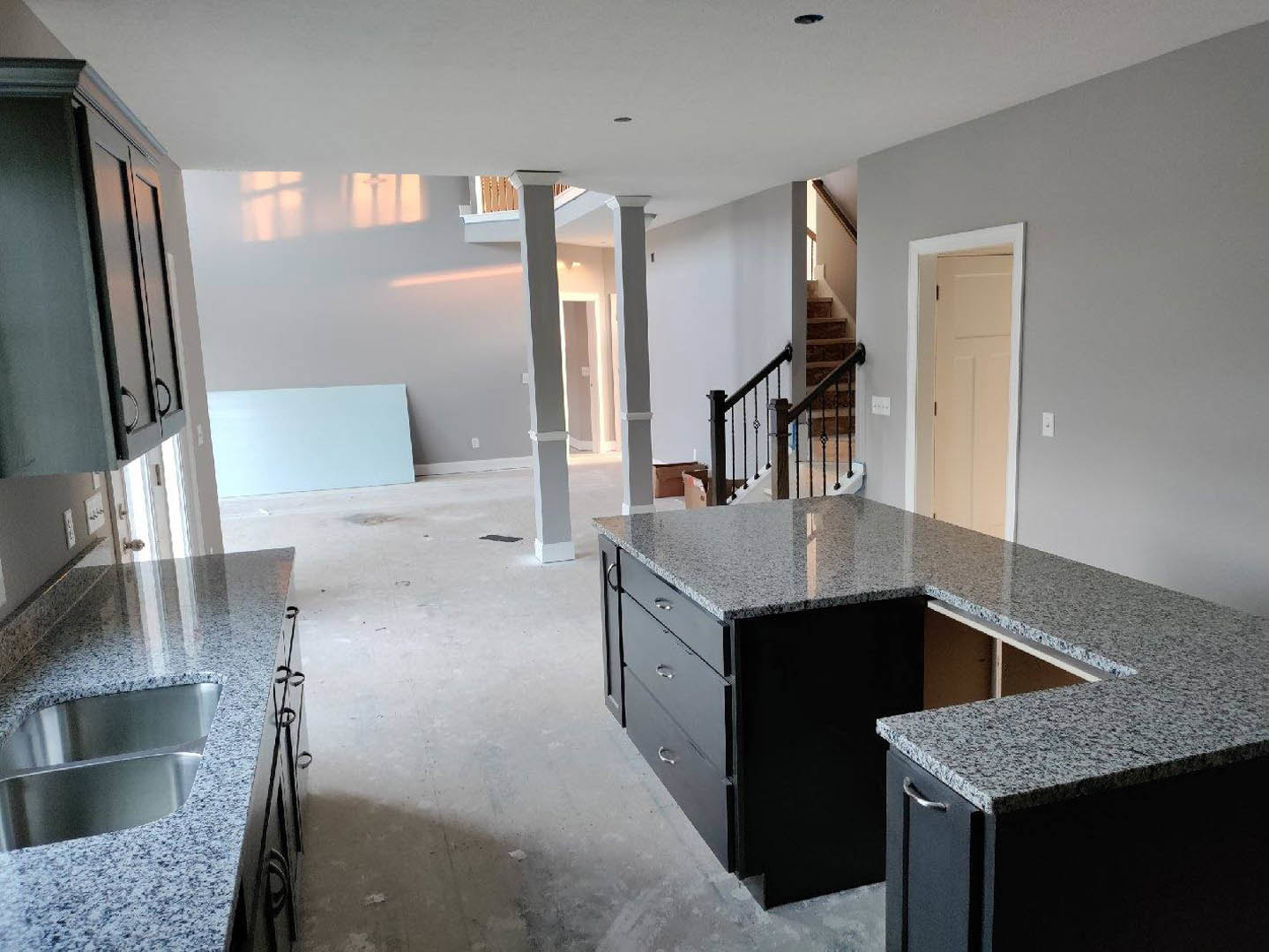 Granite kitchen countertops with stainless sink, white cabinetry, tile flooring, and adjacent staircase with wooden railing