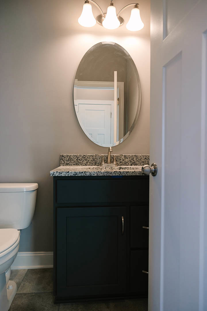 Modern bathroom featuring a large wall mirror, white tile walls, chrome faucet, open cabinet door, round door knob, and close-up of a toilet seat and light fixture