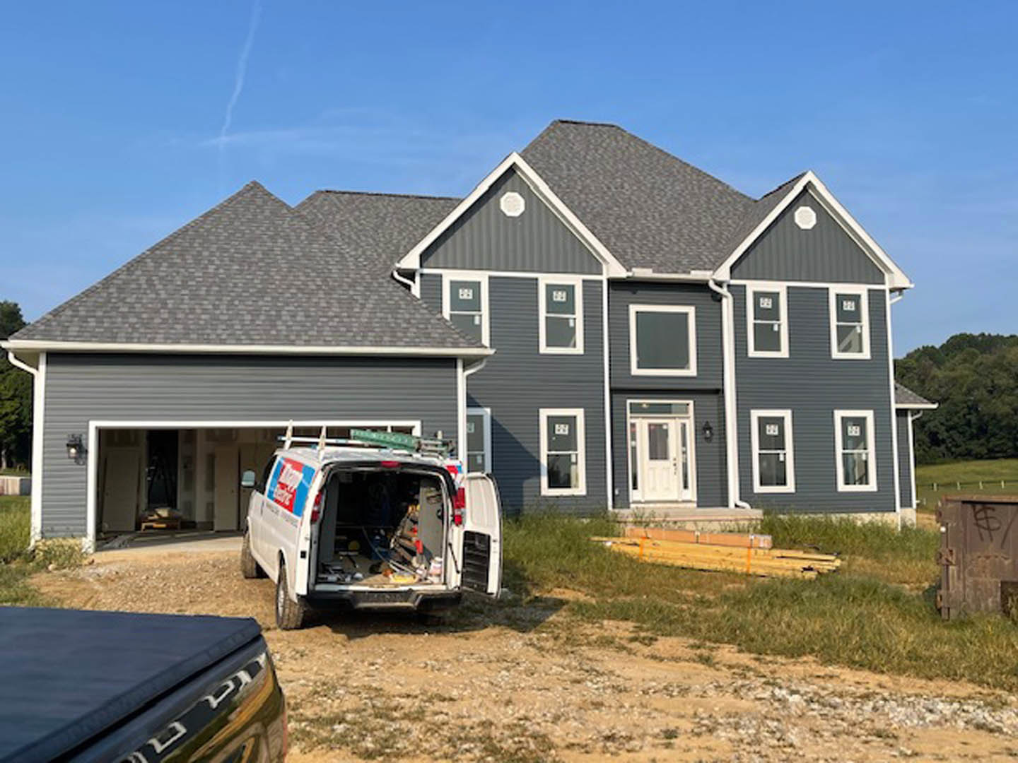 Two-story house with white siding, large windows, and a white van parked in the driveway; visible front door with glass panel and landscaped yard.