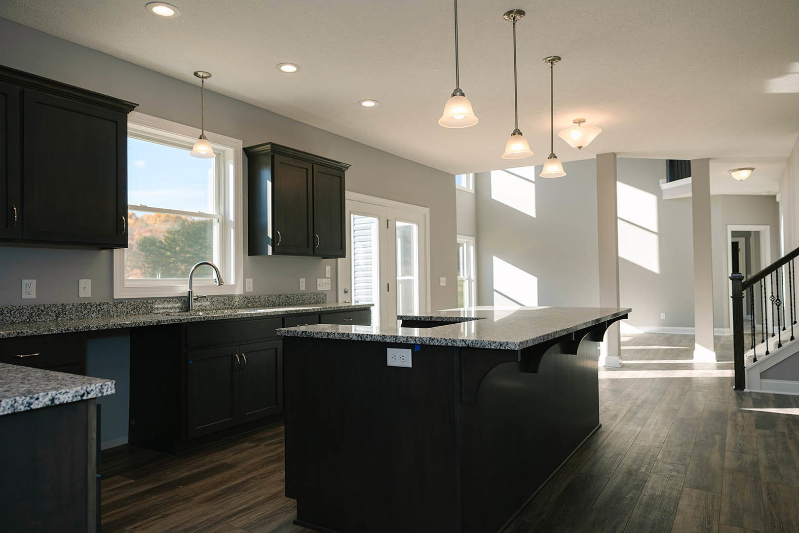 Black kitchen island with granite countertop, white cabinetry, stainless steel faucet, light wood flooring, and metal staircase railing in background