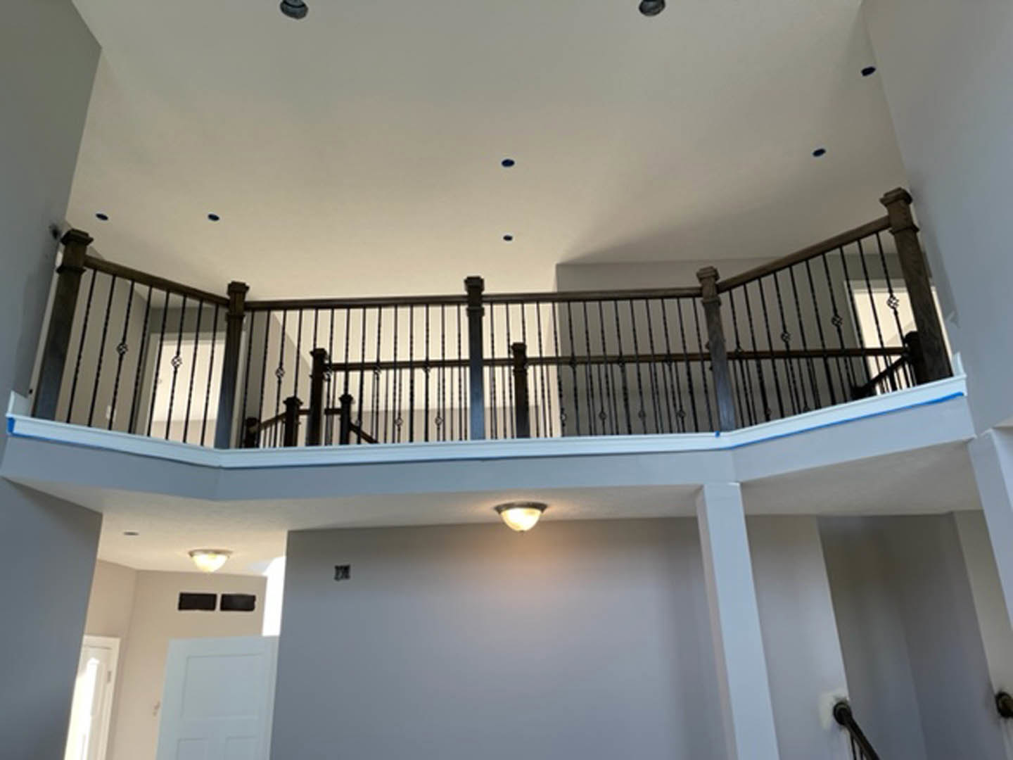 White staircase with black metal railing, white walls, open white door, ceiling light fixture, crown molding along ceiling