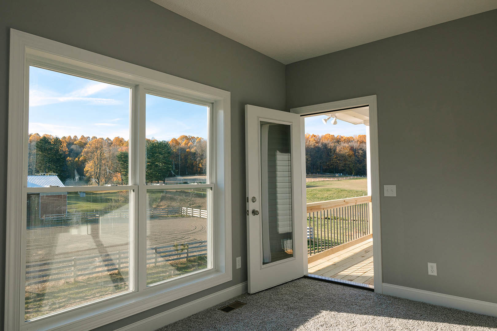 Bright room with white walls, wood flooring, large windows overlooking trees and a field, glass door opening to deck, wall vent, and close-up of paneled door