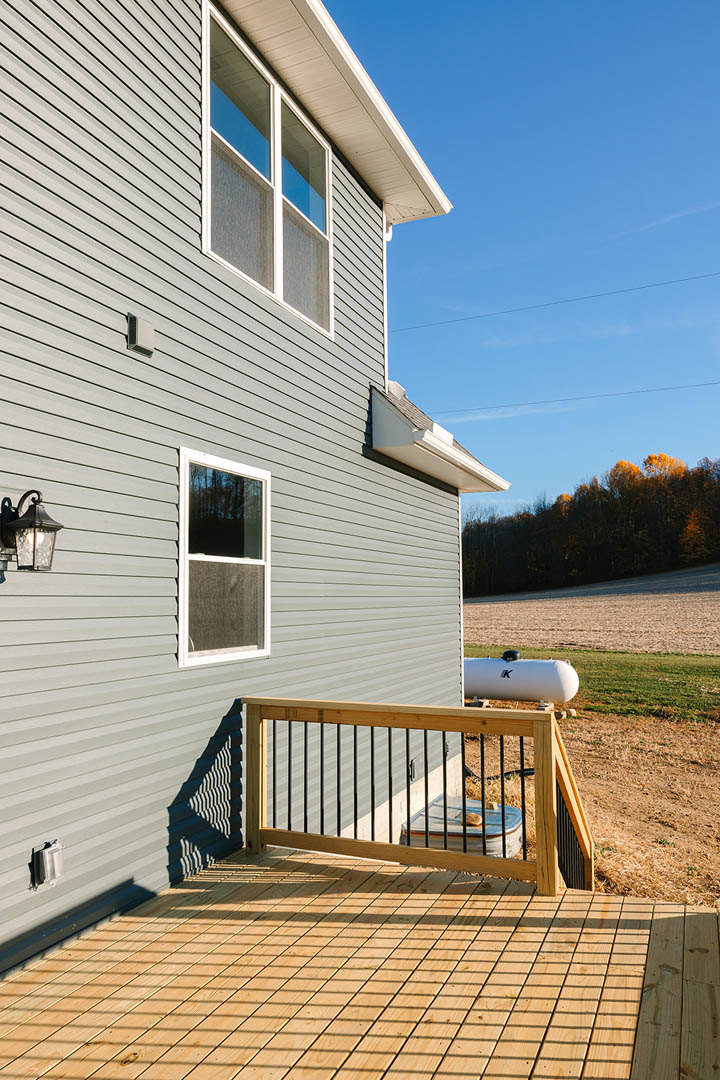 Wood deck with wooden railing, white-framed screened window, fenced yard, sunlit trees, light-colored siding exterior