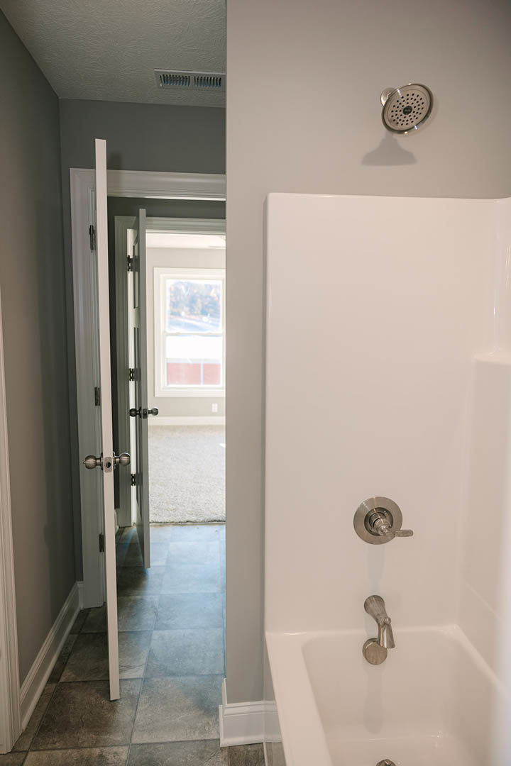 Freestanding white bathtub with chrome faucet and handle, surrounded by light gray tile walls and a large wall mirror in a modern bathroom