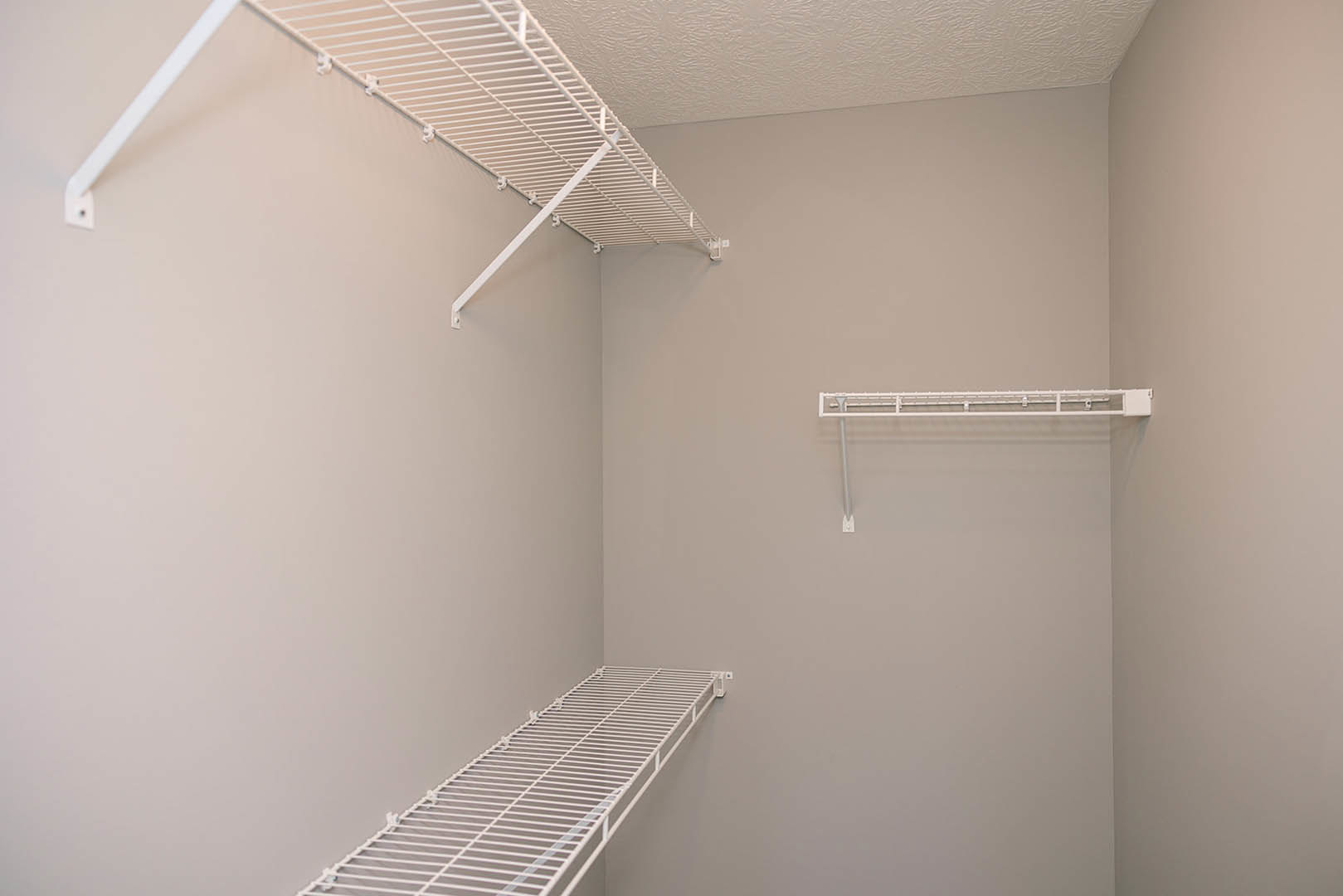 White wire shelf with hooks mounted on a plaster bathroom wall, illuminated by overhead lighting.