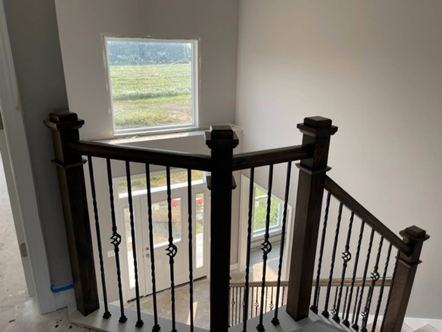 Modern staircase with black metal handrail and balusters, large window overlooking grassy field, light wood flooring