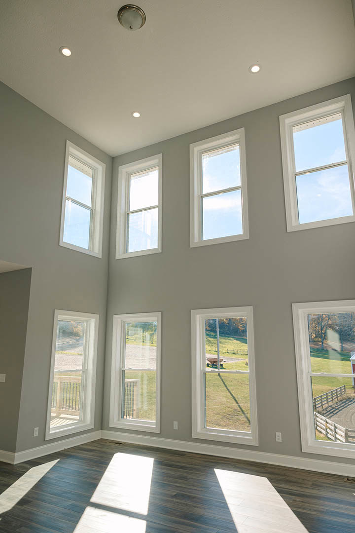 Spacious room featuring multiple large windows, light streaming onto polished wooden floors, white walls, and views of grassy yard with fence and blue sky.