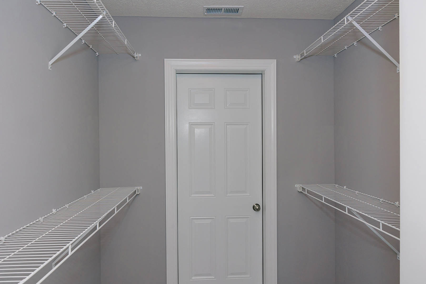 White closet with built-in white shelves, white door featuring a silver handle, metal bars supporting shelving, white plaster walls.