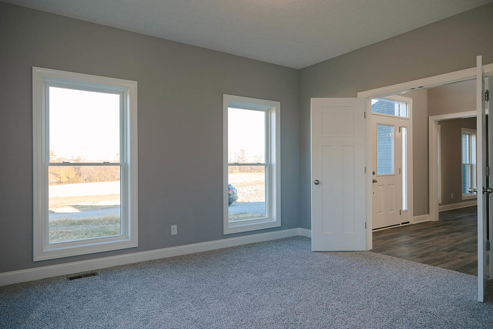 Carpeted room with white walls, large window overlooking a field, and a white door featuring a silver knob and glass panel