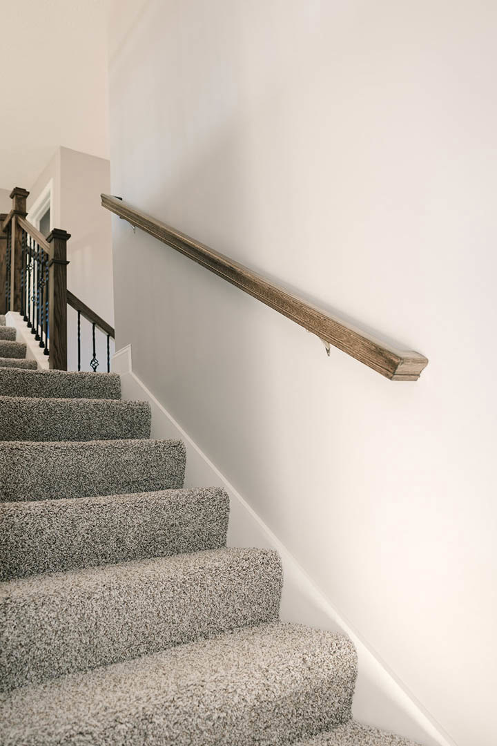Carpeted staircase with wooden handrail and balusters against a painted wall