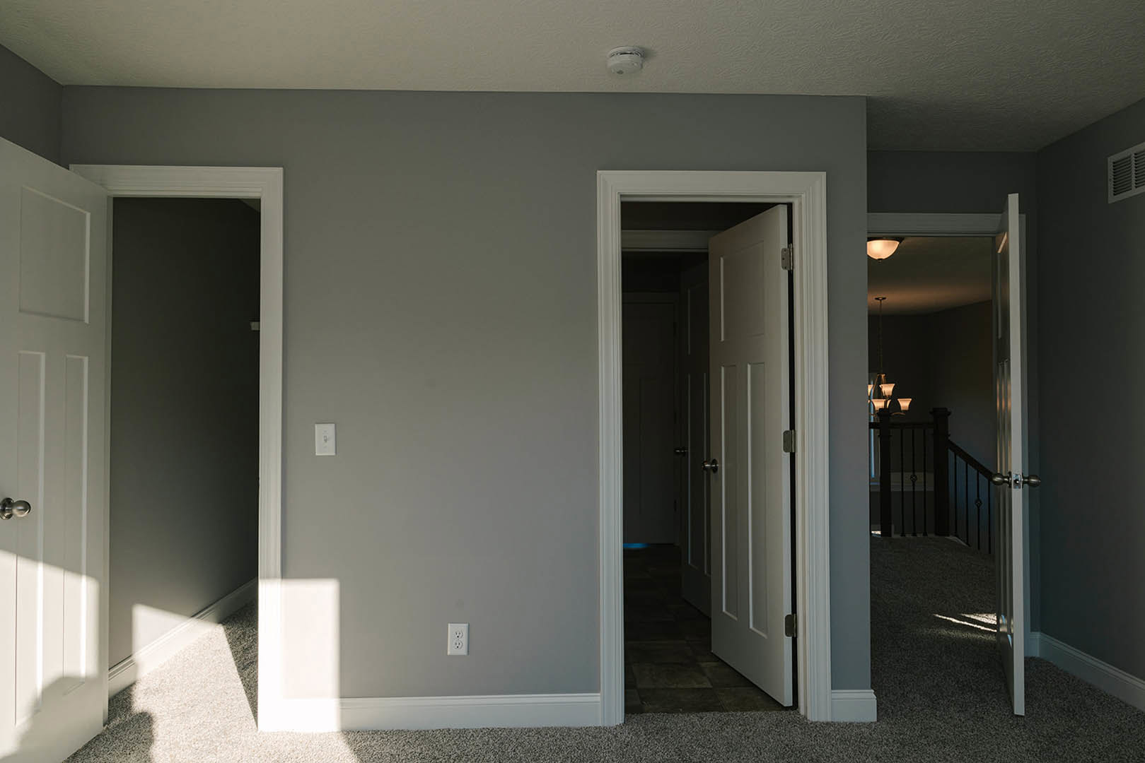 White paneled door with silver knob open to a room, smoke detector and air vent visible on white ceiling and wall, light-colored flooring