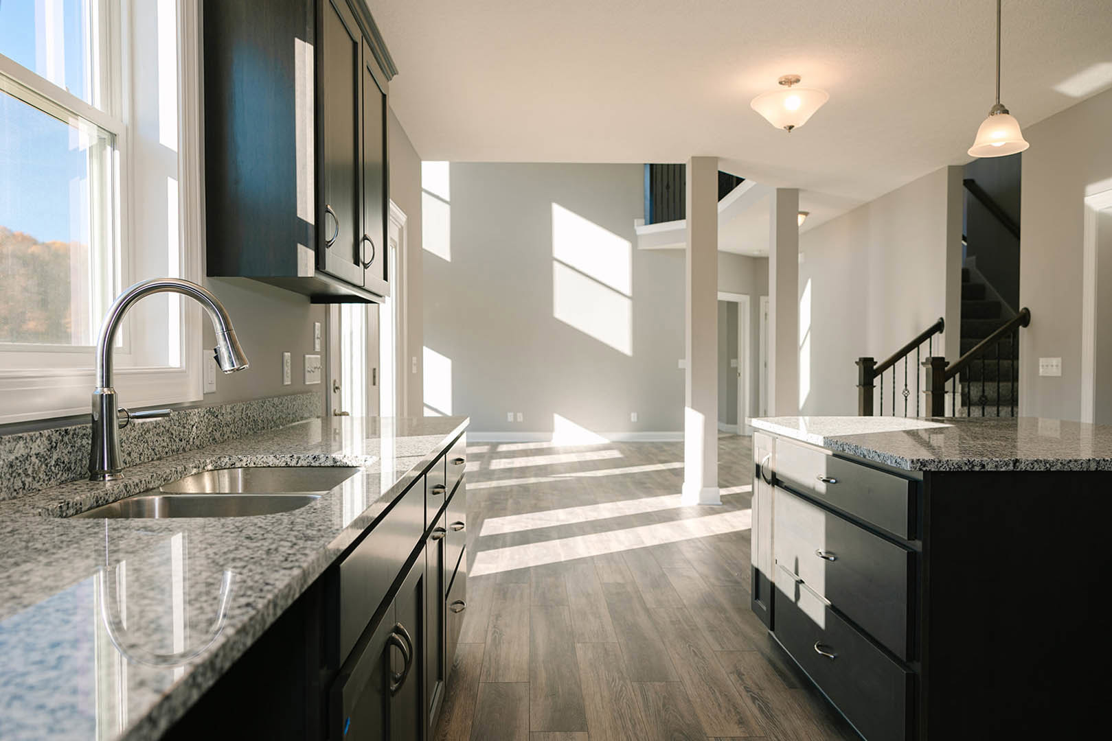 Kitchen with polished granite countertops, wood flooring, stainless steel faucet and sink, large window, modern pole-mounted light fixture, and tile backsplash.