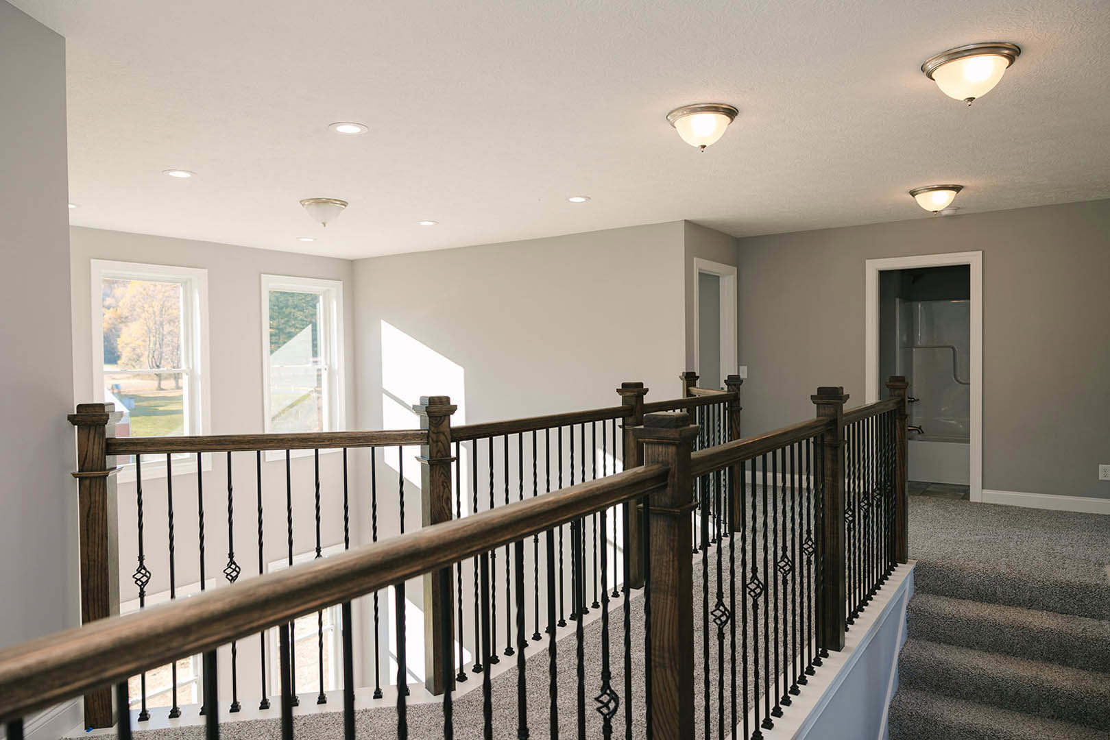 Wood staircase with metal balusters, white plaster walls, hardwood floor, recessed ceiling light, and a nearby window with trim.