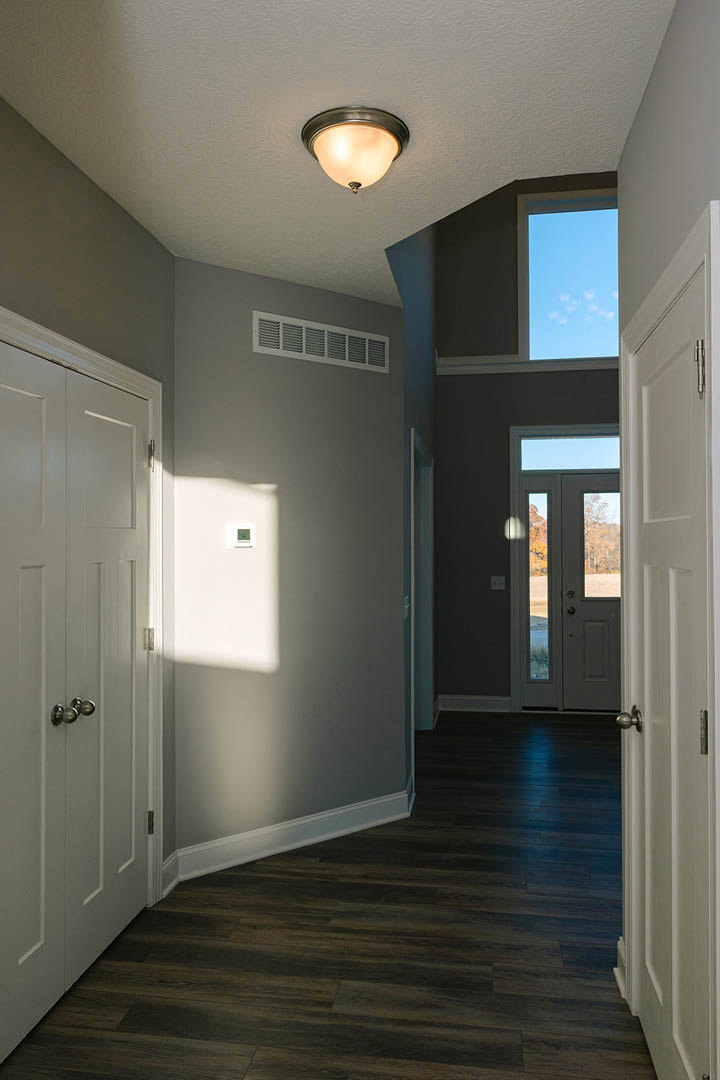 Hallway with dark wood flooring, white trim, multiple white paneled doors, ceiling-mounted light fixture, wall vent, smooth plaster walls