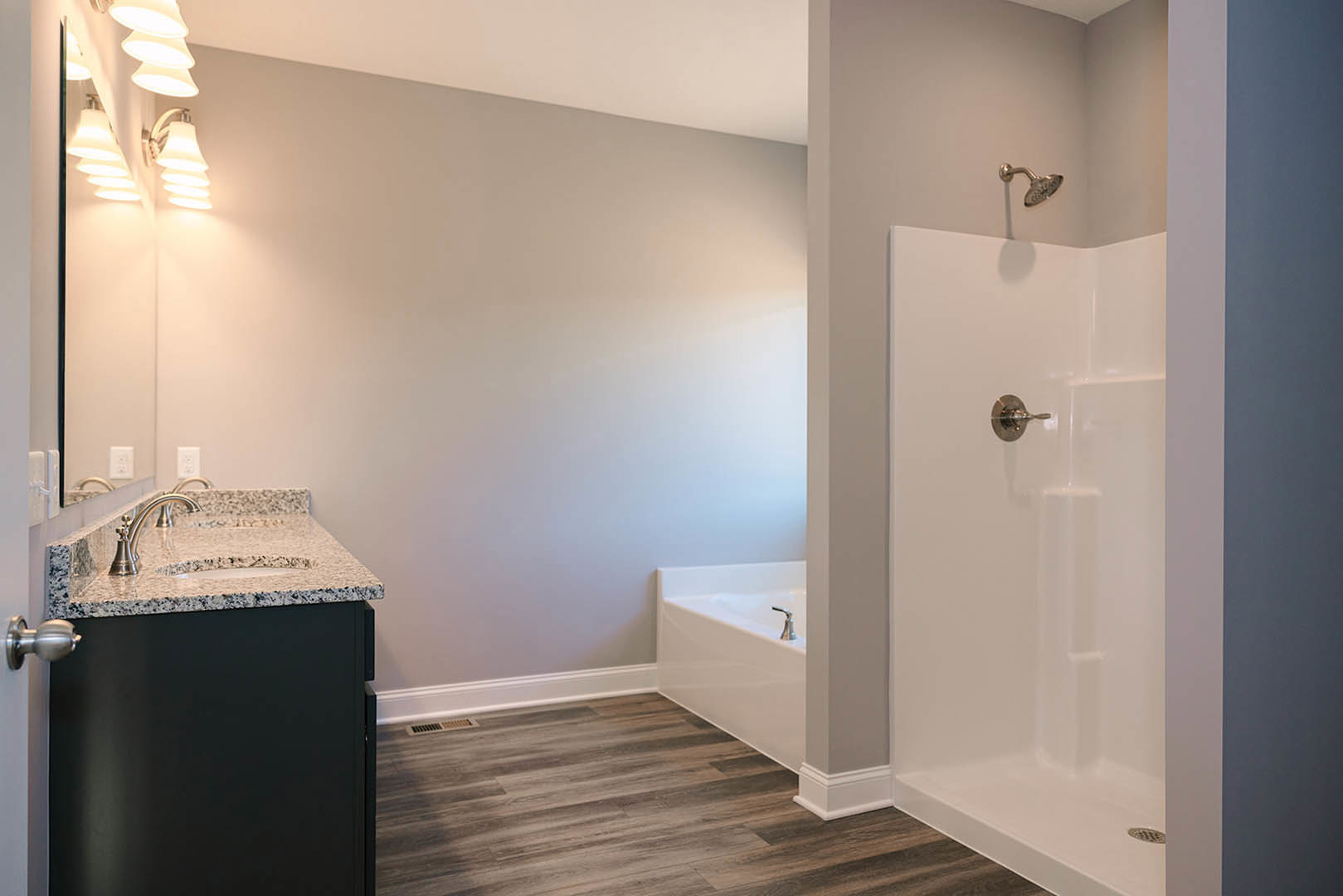 Modern bathroom featuring a freestanding white bathtub, glass-enclosed shower with silver handle, white tile walls, light wood cabinetry, wall-mounted lights, and chrome fixtures.