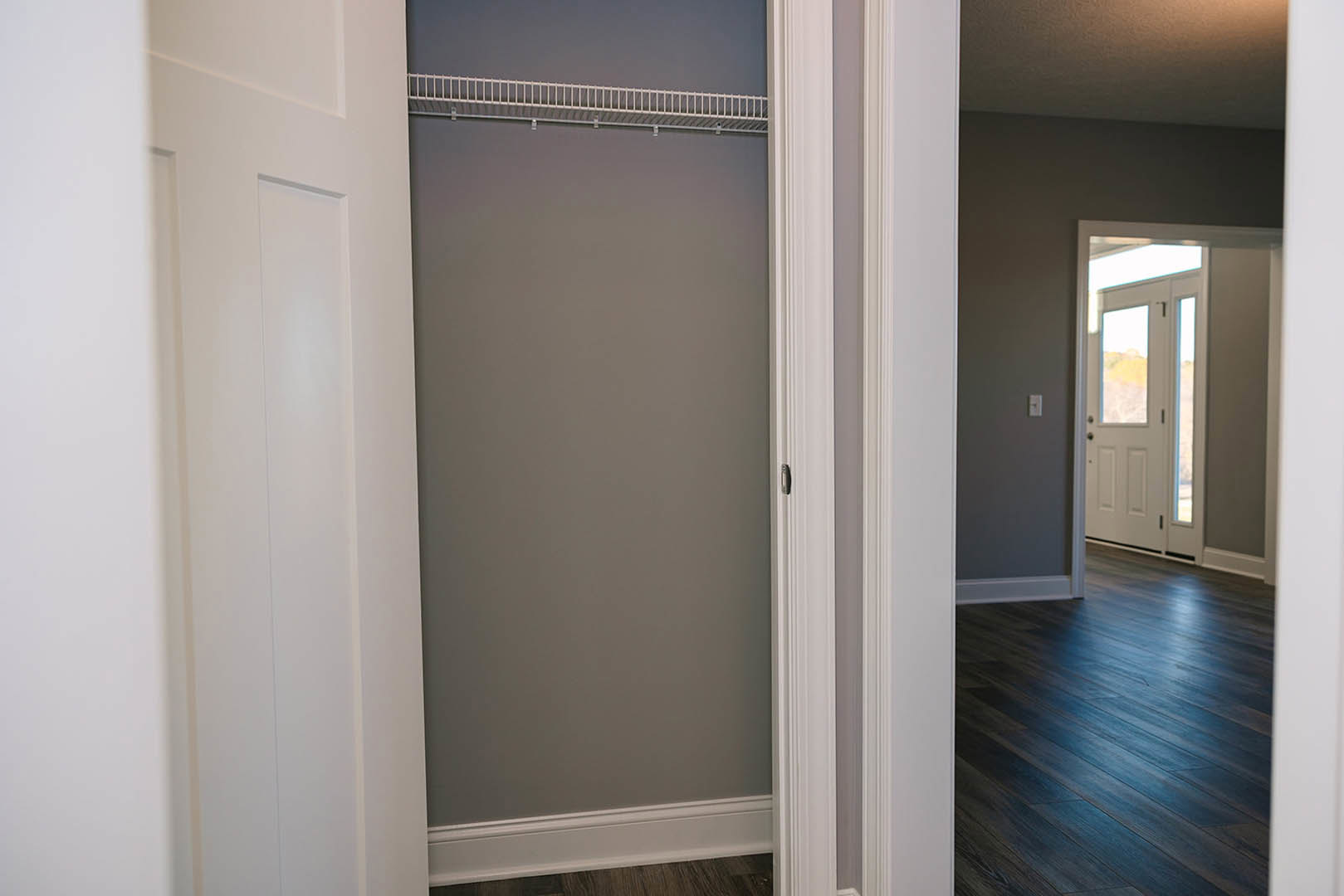 Walk-in closet with grey walls, white framed glass door, dark wood flooring, white ladder leaning against wall, and white baseboard trim