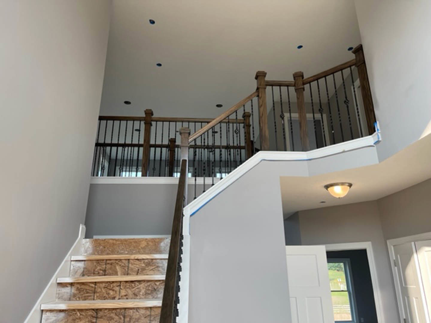 Wood staircase with blue LED accent lighting, white balusters and handrail, modern pendant light fixture illuminated above, white door with sunlight streaming through, window on